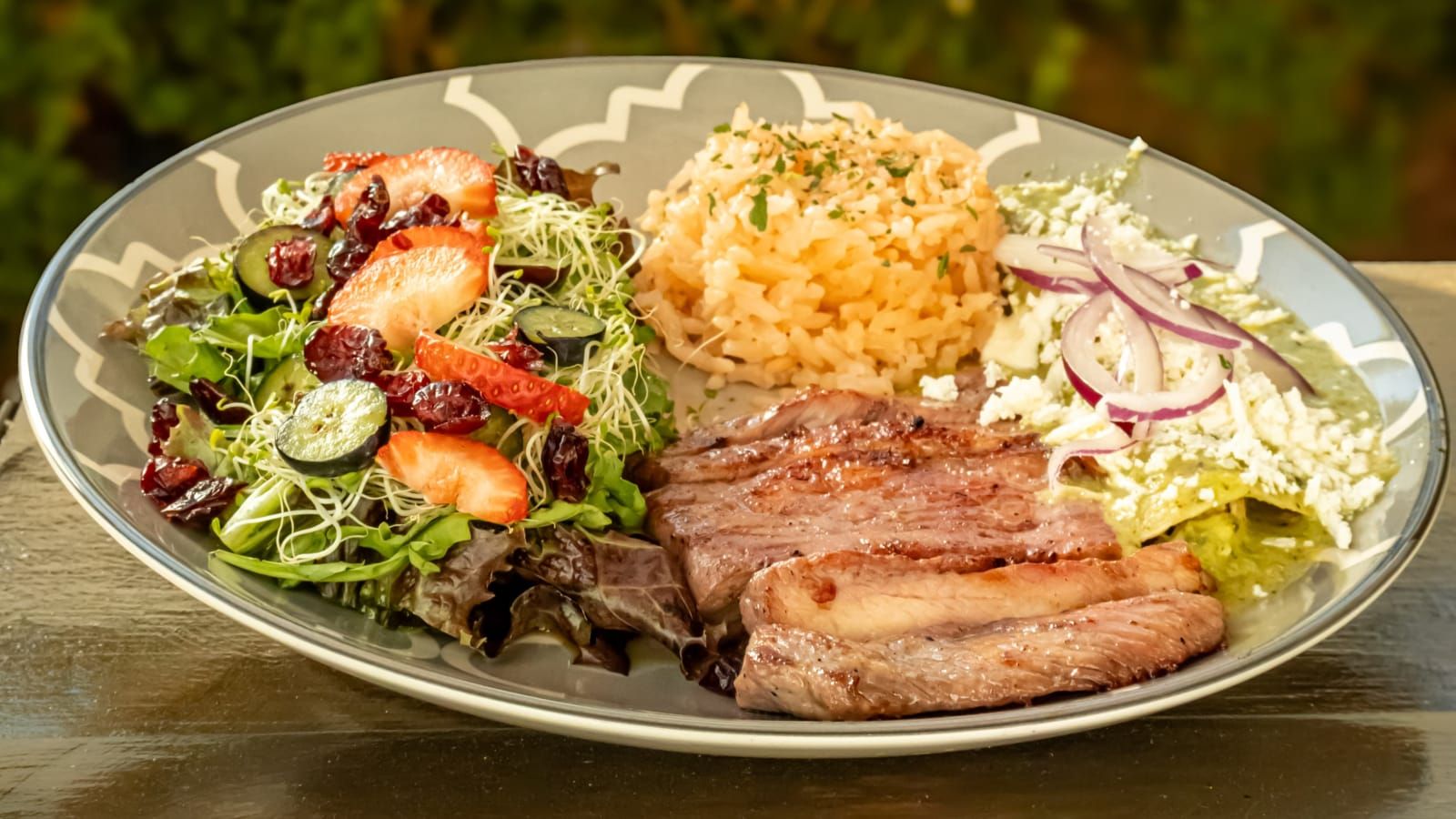 Platillo de carne con ensalada y una flor sobre la mesa